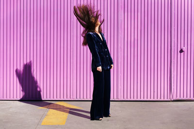 Full length of woman standing against pink wall outdoors