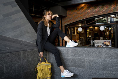 Portrait of businesswoman with backpack sitting on retaining wall