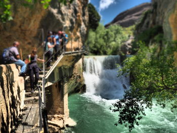 People on rock by waterfall against sky