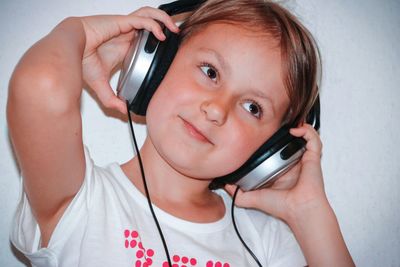 Girl looking away while listening music against wall at home