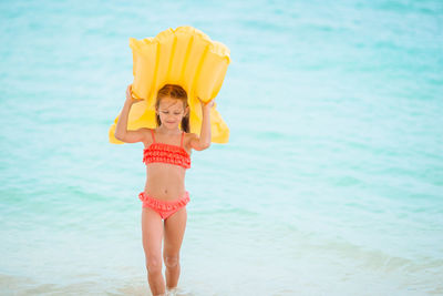 Girl carrying swimming float while waking in sea