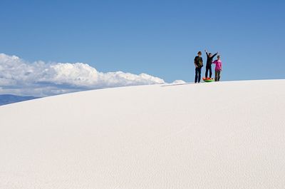 Friends standing on snow covered hill against blue sky during sunny day