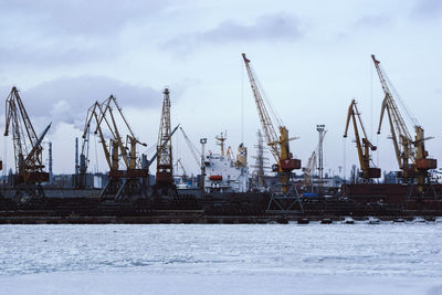 Cranes at commercial dock against sky during winter