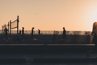Silhouette people standing on railing against orange sky