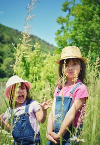 Portrait of smiling girl with sister standing by plants on field 