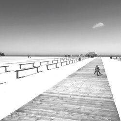 Rear view of boy riding bicycle on pier at beach against sky