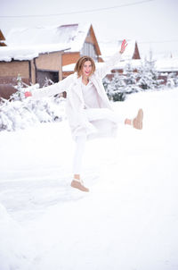 Portrait of smiling woman standing with arms outstretched on snow covered land