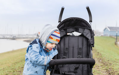 Girl wearing warm clothing looking at baby stroller on field