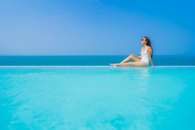Young woman relaxing at infinity pool against sea