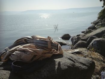 Man relaxing on rocks by sea against sky