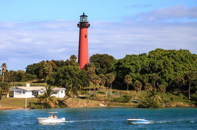 Lighthouse by sea and buildings against sky