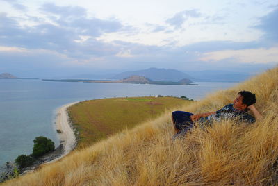 Man looking at sea while lying on mountain against sky