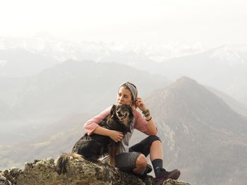 Young woman sitting on rock against mountain