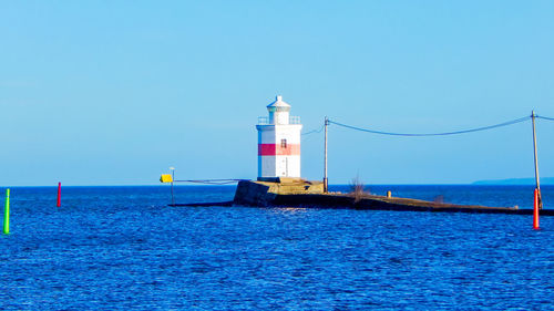 Lighthouse by sea against clear sky