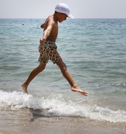 Side view of playful shirtless boy jumping on shore at beach