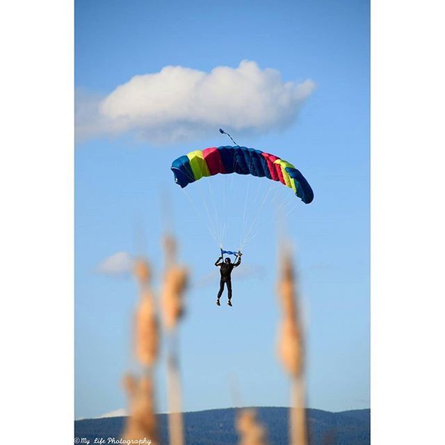 flying, mid-air, low angle view, sky, transportation, extreme sports, parachute, national flag, air vehicle, flag, multi colored, mode of transport, cloud - sky, freedom, patriotism, adventure, kite, blue, sport, kite - toy