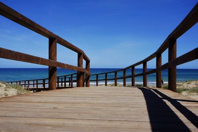 Footbridge over sea against clear blue sky