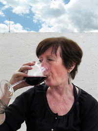 Senior woman drinking wine against wall