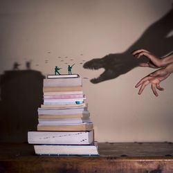 Cropped image of hands making dinosaur shadow attacking on soldier figurines on books