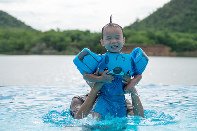 Woman lifting boy wearing water wings in swimming pool