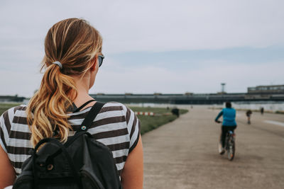 Rear view of woman riding bicycle on road against sky