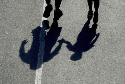 Low section of man with son walking on road during sunny day