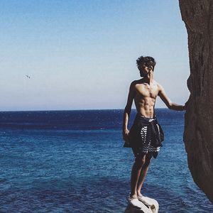 Full length of shirtless man standing in rock against clear sky