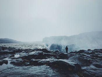 Rear view of person standing on cliff against sky during foggy weather