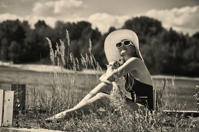 A woman in a swimsuit, hat and sunglasses sunbathes in summer on the riverbank among the grass