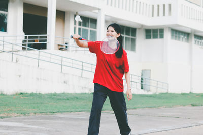 Smiling young woman playing badminton while standing outdoors