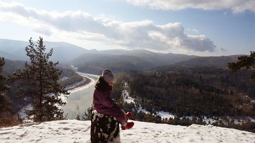 Girl wearing warm clothing while sitting on snowcapped mountain during winter