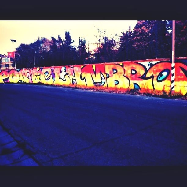 yellow, multi colored, graffiti, transportation, illuminated, art, night, street, tree, road, creativity, text, outdoors, no people, art and craft, clear sky, road marking, built structure, wall - building feature, orange color