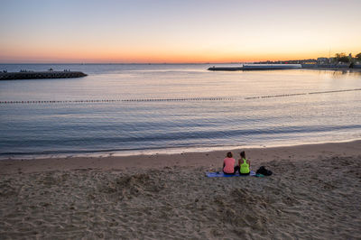 High angle view of friends sitting at beach against clear sky during sunset