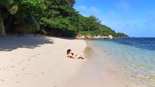 Full length of woman sunbathing on sandy beach.