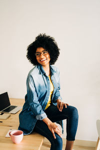 Portrait of smiling young woman using phone while sitting on table