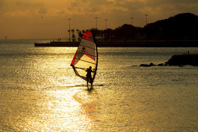 Silhouette person windsurfing in sea during sunset