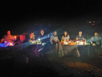 People sitting by illuminated fire at night