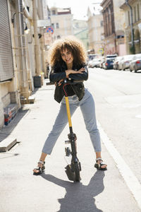 Portrait of smiling teenage girl standing with scooter on pavement