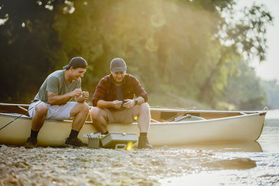 Friends adjusting fishing tackles while sitting on boat by lake