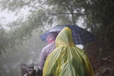 Men in raincoat holding umbrella by trees