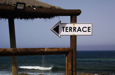 Information sign by sea against clear sky