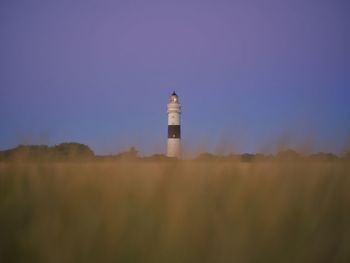 Lighthouse on field by building against sky