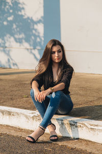 Young woman looking away while sitting on footpath