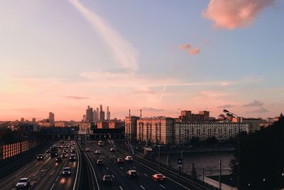 High angle view of cars moving on street by buildings against cloudy sky during sunset