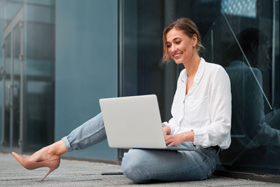 Woman using mobile phone while sitting on laptop