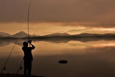 Silhouette man standing on shore against sky during sunset