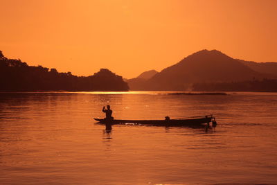 Silhouette person on boat over lake against clear sky