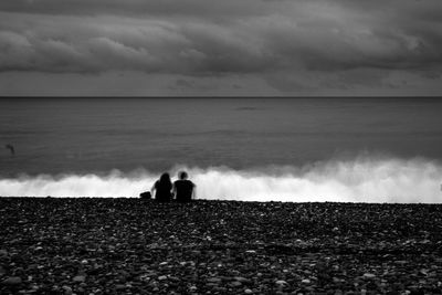 Rear view of couple at beach against cloudy sky