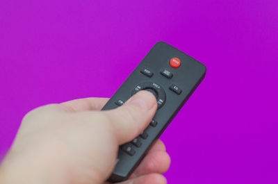 Cropped hand holding remote control against blue background