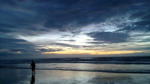 Silhouette people on calm beach at sunset